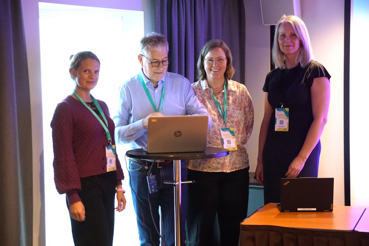 Fem mennesker står rundt et bord med pc