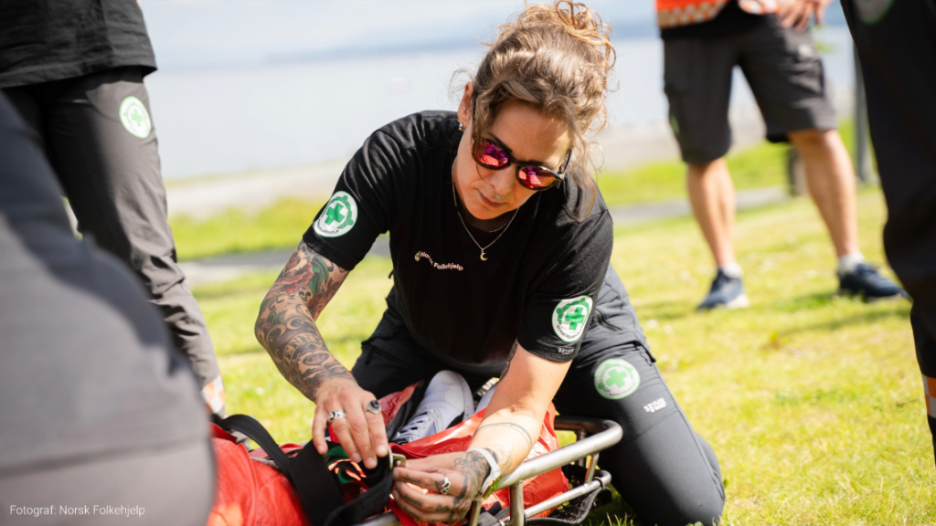 Kvinne fra norsk folkehjelp fester pasient på båre