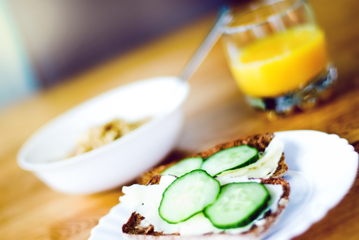Brødskive med agurk, glass med appelsinjuice og skål med frokostblanding.