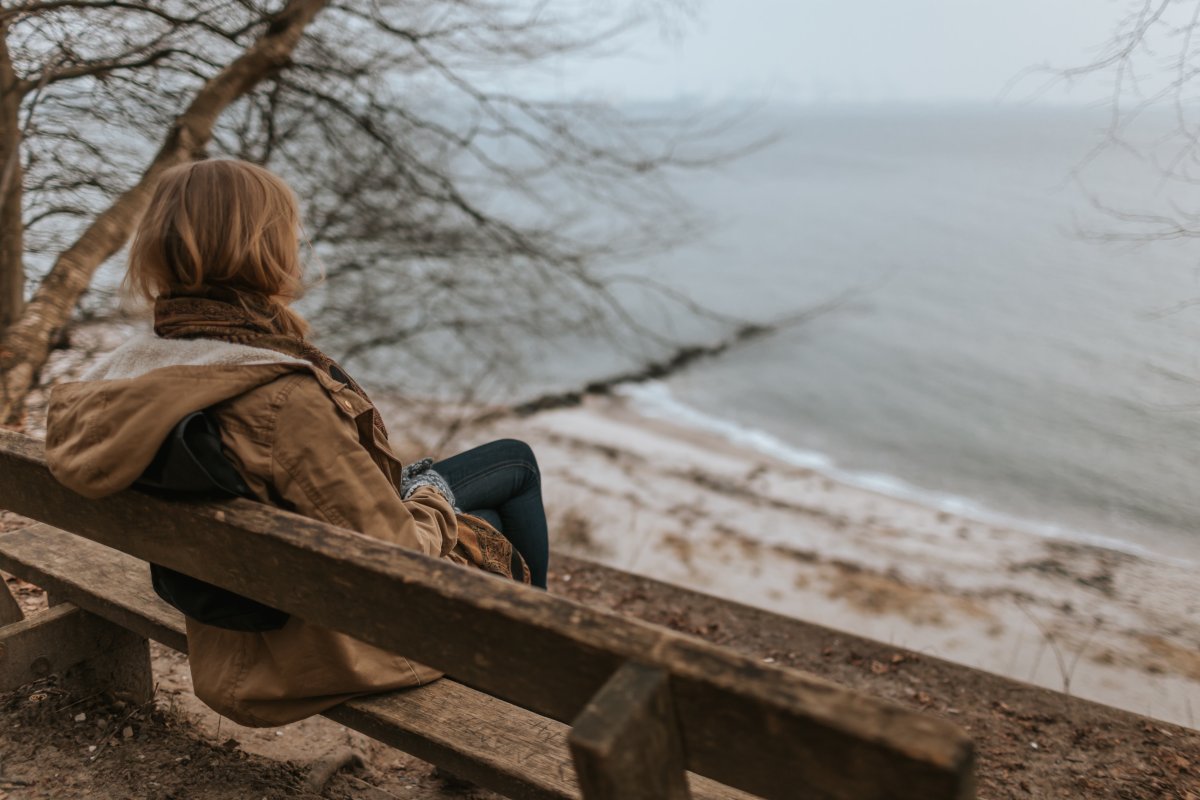 Illustrasjonsbilde - trist kvinne sitter alene på benk og ser utover havet. Foto: Unsplash
