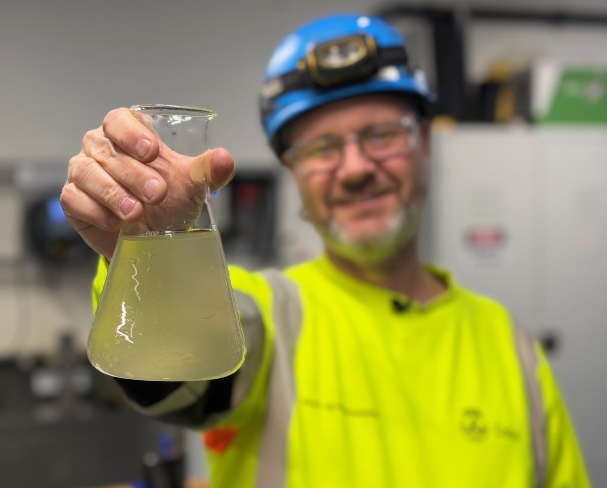 Mann i bakgrunnen holder opp et glass med innhold 