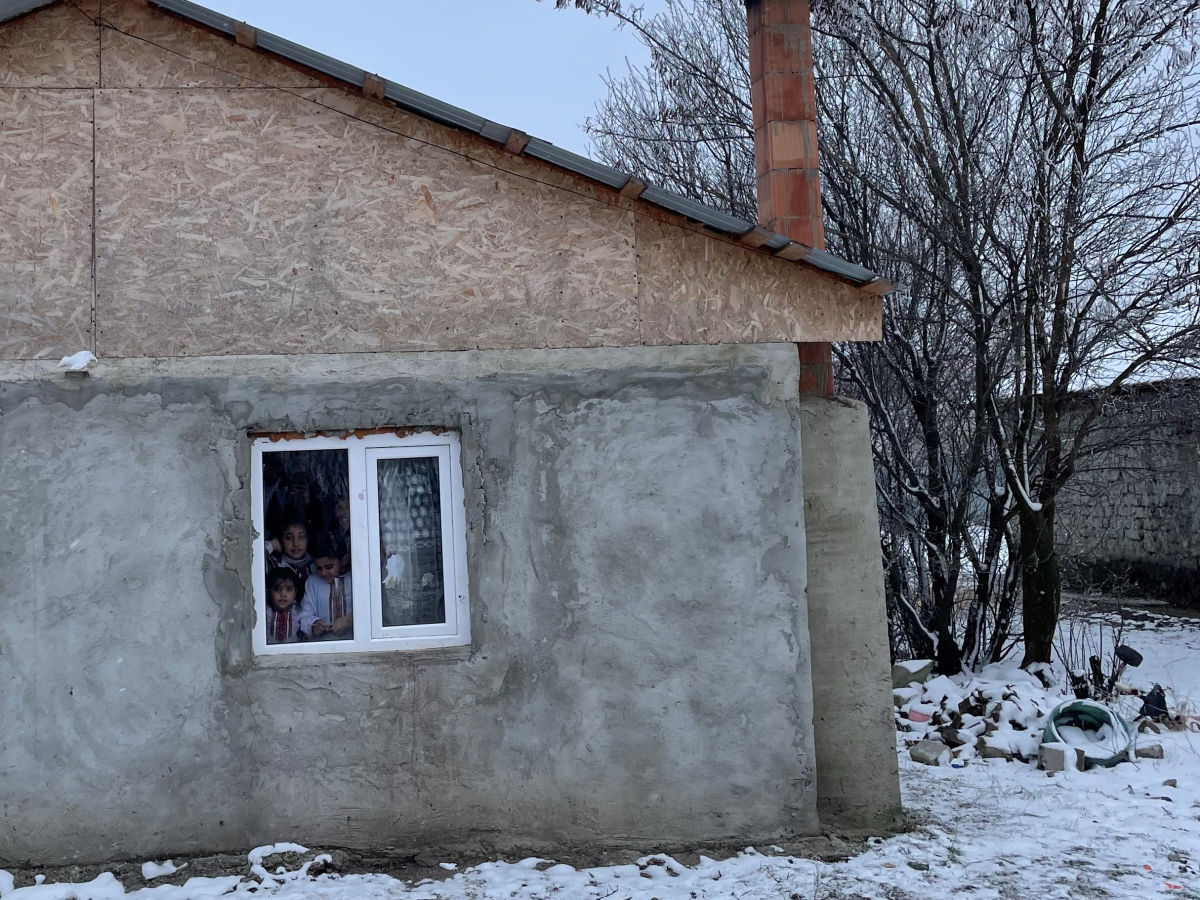 3 barn titter ute av vinduet i et hus i Romania i byen Dragoș Vodă.