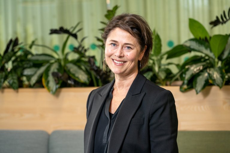 Divisjonsdirektør analyse og samfunn Helen Brandstorp smiler foran grønn bakgrunn.