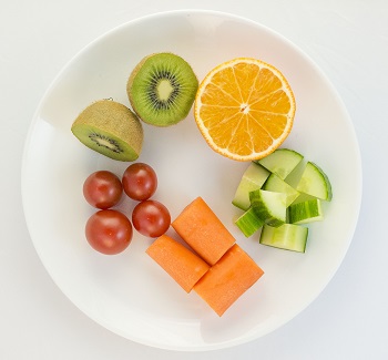 Tomater, kiwi, appelsin, agurk og gulrot på et hvitt fat.