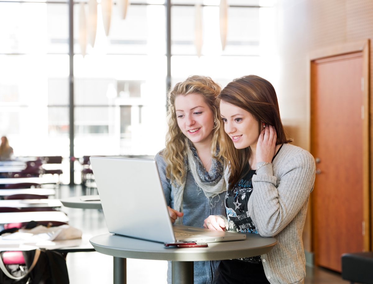 To unge kvinner står ved et bord i et kontorlandskap og ser på en datamaskin